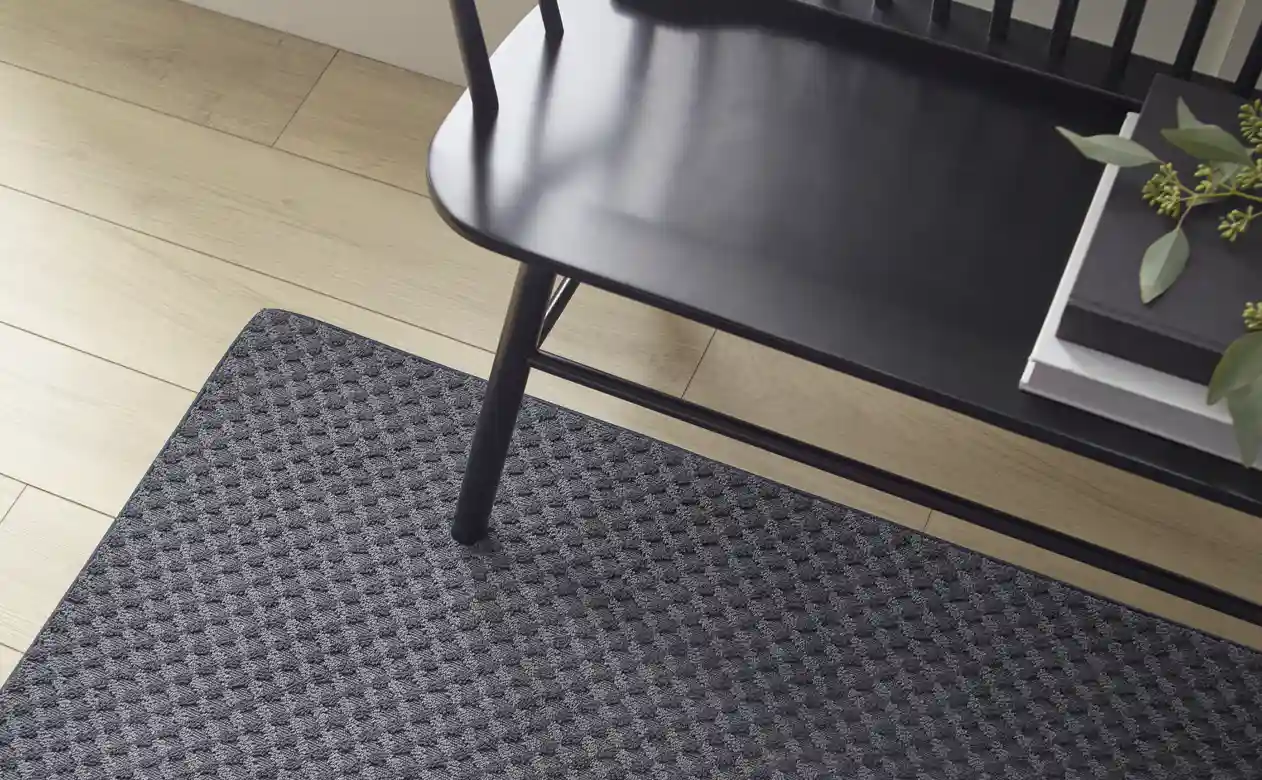 Grey area rug in entryway, below a black wooden bench.